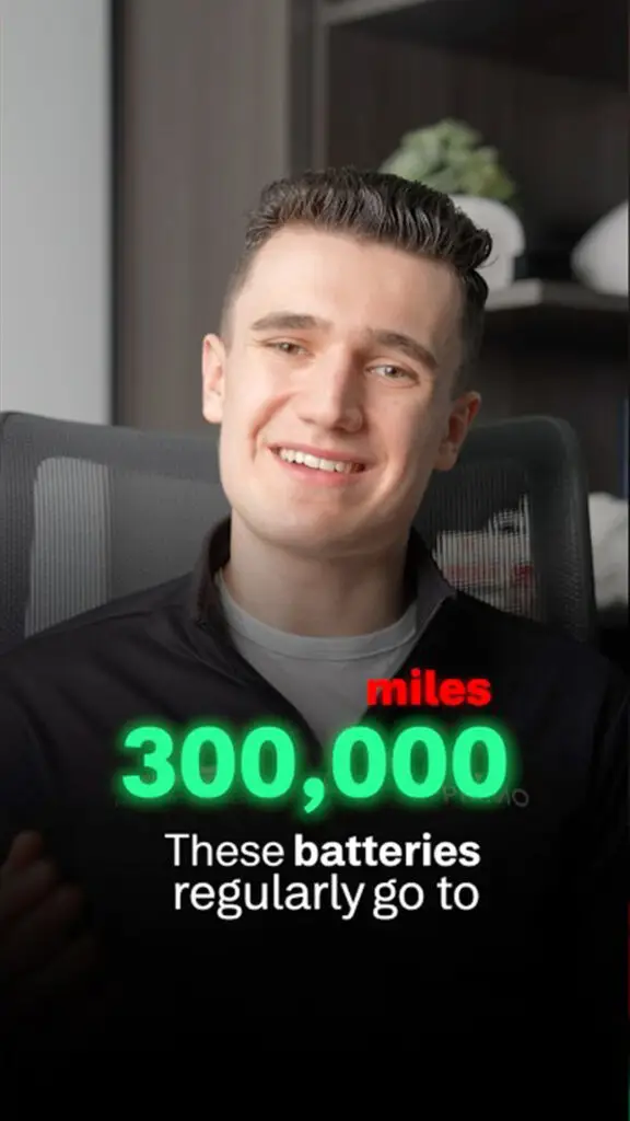 Smiling man in a dark jacket holding a sign that reads '300,000 miles' in bright green, about battery milestones.