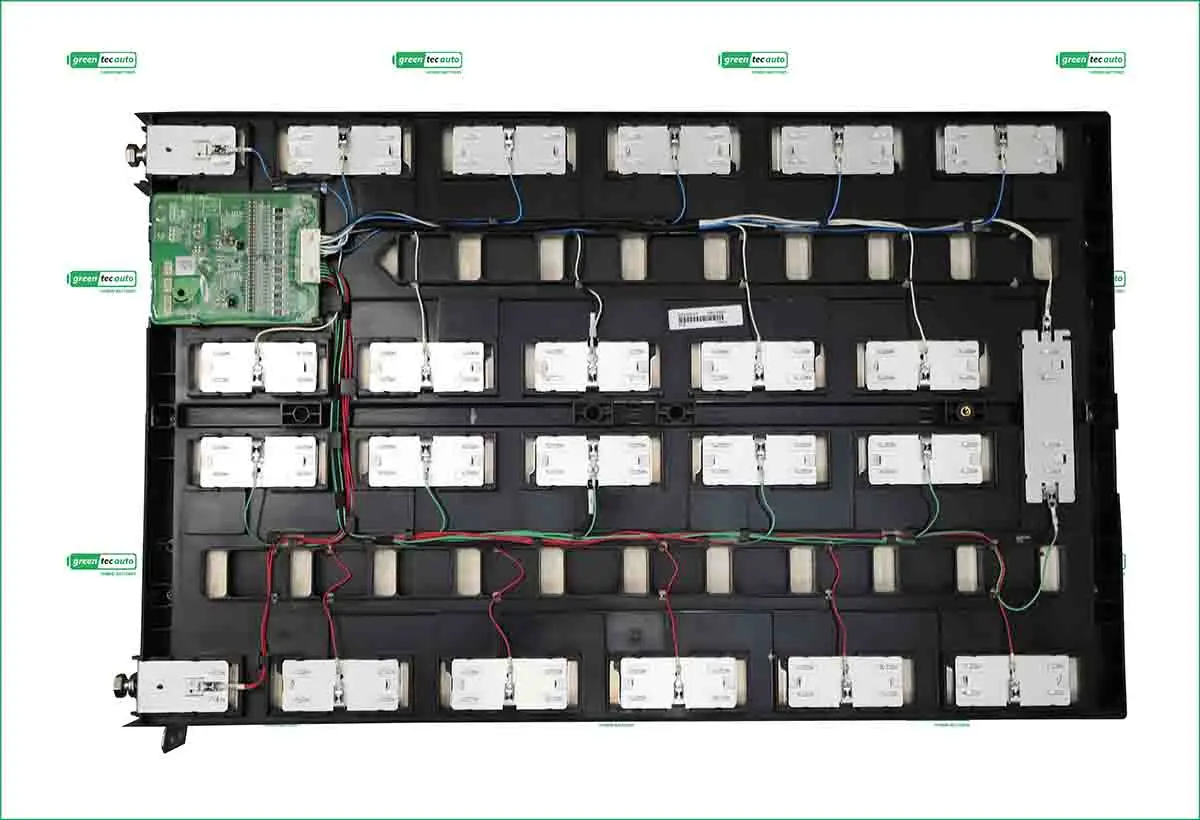 Interior view of a large battery pack showing rows of rectangular cells connected by red and black wires and a green control circuit on the left.