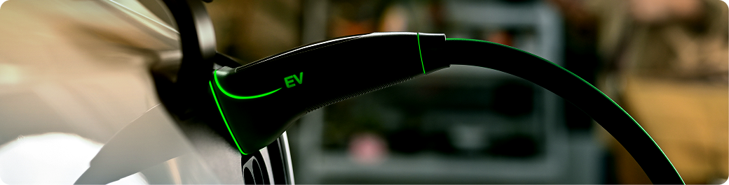 Close-up of an EV charging plug with a green 'EV' label on the handle.
