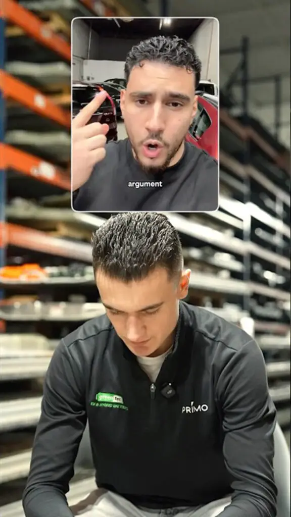 Man in a black Primo polo seated in a warehouse, looking down at something, shelves in the background