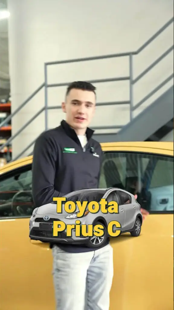 Salesperson in a dark jacket stands beside a yellow car in a dealership, with a large 'Toyota Prius C' overlay image in front of him.